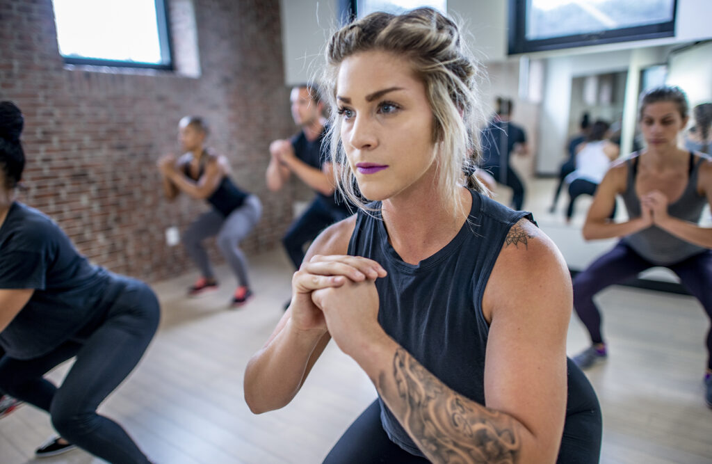 Diverse group of young adults doing squats in unison during a fitness class