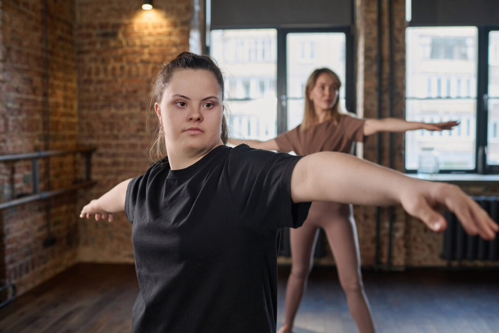 Young active woman with Down syndrome in black t-shirt outstretching arms during physical exercise while standing in front of camera