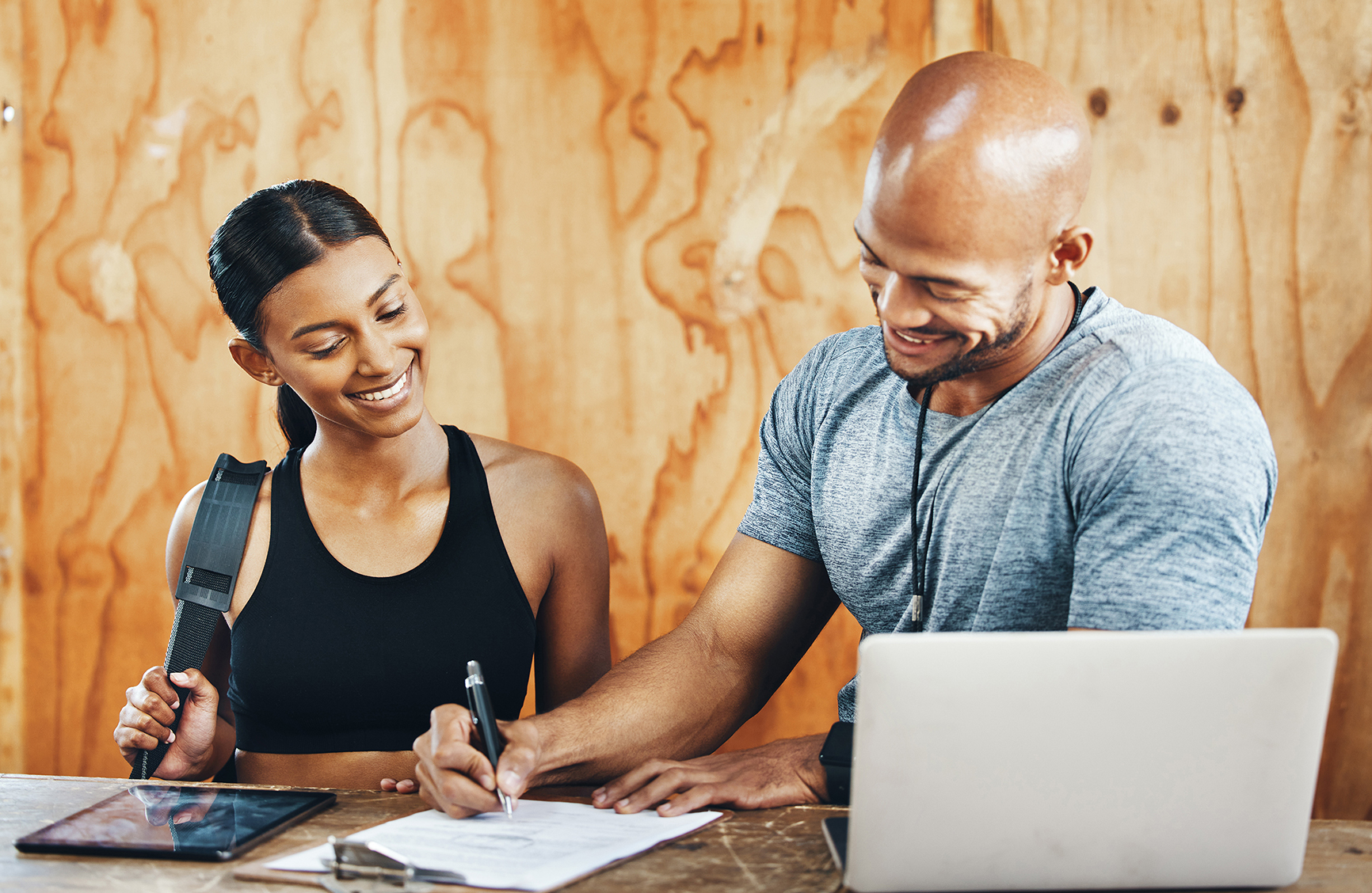 Shot of a young man filling out paperwork while assisting a client in a gym