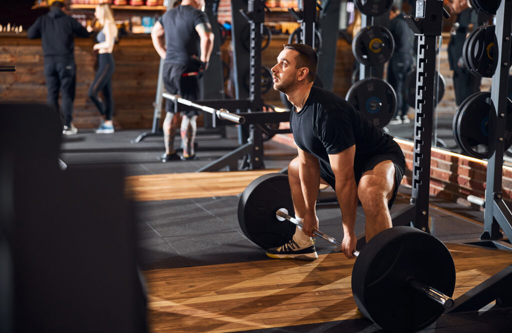 Focused male athlete in sports clothes squatting while trying to lift a heavy barbell